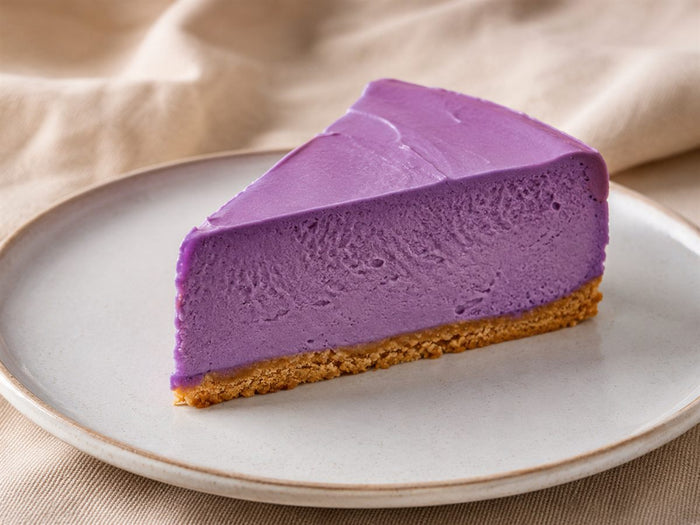 Part de cheesecake a l'ube violet, base biscuit doree, assiette claire, fond lin