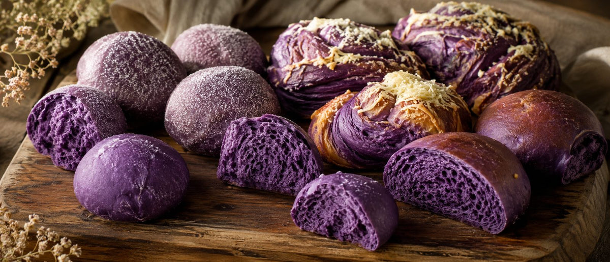 Assortiment de pains et brioches philippins à l'ube, mie violet magenta, sur planche de boulangerie