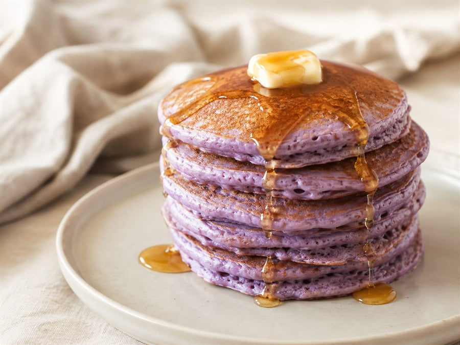 Pile de pancakes a l'ube violets, sirop d'erable, beurre, assiette claire, fond lin