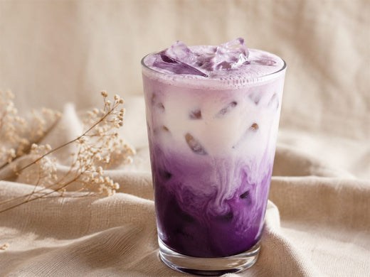 Iced latte signature a l'ube, degrade violet sur glacons, mousse soyeuse, fond lin premium